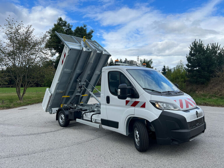 Benne basculante blanche avec bras hydraulique levé. Camion utilitaire pour travaux.