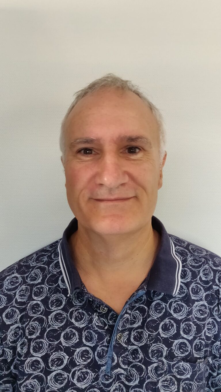 Portrait d'un homme souriant portant une chemise bleue à motifs.