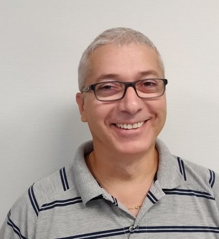 Homme souriant avec des lunettes, portant un polo rayé gris et bleu.