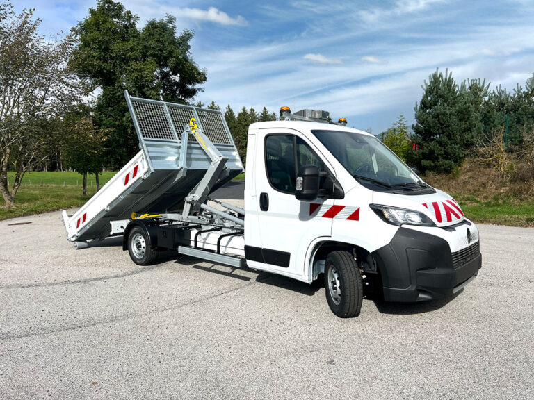 Camion benne blanc avec bras hydraulique levé, ciel bleu en arrière-plan.
